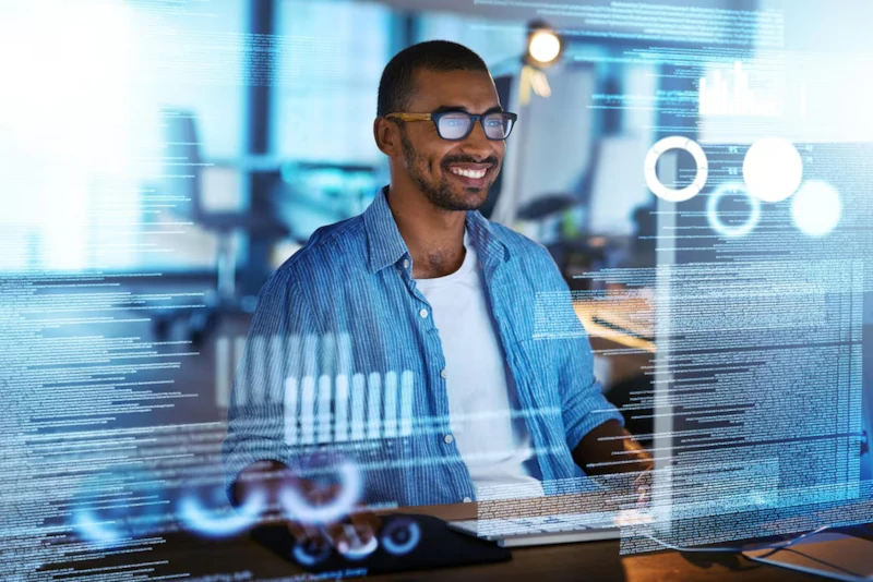 Hombre sonriendo frente a computadora con códigos de programación