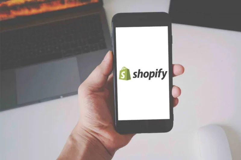 Mano sujetando teléfono con logo de Shopify